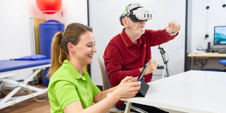 Eine Therapeutin unterstützt bei der VR-Therapie, während ein Patient damit gezielt seine neurokognitiven und motorischen Fährigkeiten schult.