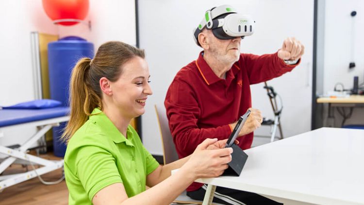 Eine Therapeutin unterstützt bei der VR-Therapie, während ein Patient damit gezielt seine neurokognitiven und motorischen Fährigkeiten schult.