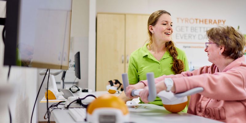 Eine Therapeutin zeigt einer Patientin, wie sie ihre Arme trainieren kann.
