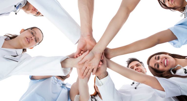 Ärzte, Ärztinnen und Pflegekräfte stehen im Kreis und halten in der Mitte die Hände aufeinander